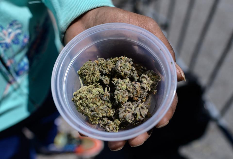 A container of marijuana buds are held up to the camera.
