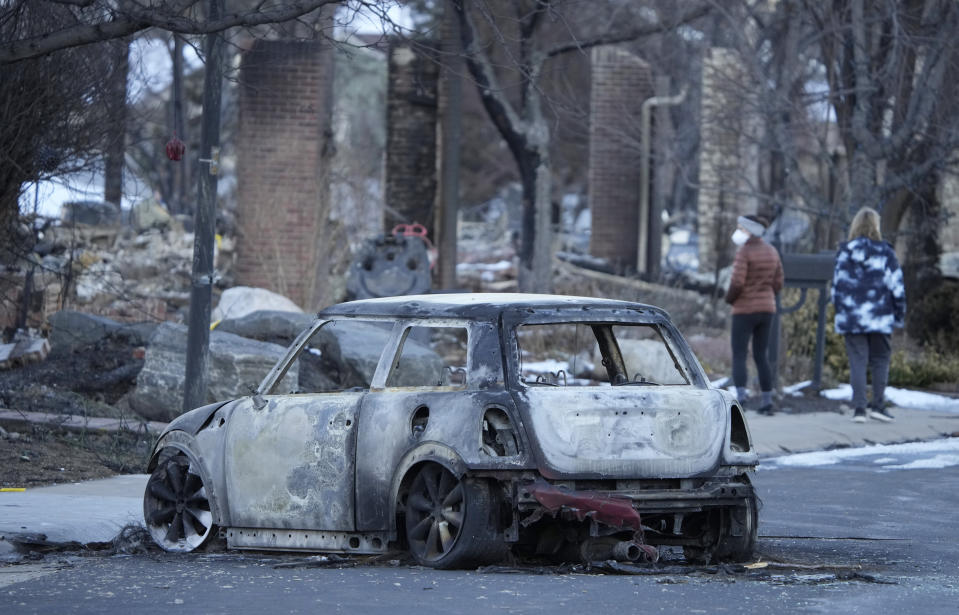 File—A charred Mini Cooper sits in Mulberry Street as pedestrians walk amid the rubble of homes destroyed by wildfires Tuesday, Jan. 4, 2022, in Louisville, Colo. Just over a year after the most-destrucctive wildfire in the state's history, a bill is being introduced in Colorado's Legislature to create a $2-million pilot program to use cameras likely equipped with artificial intelligence technology in high-risk areas to help identify fires before they can burn out of control. (AP Photo/David Zalubowski, File)