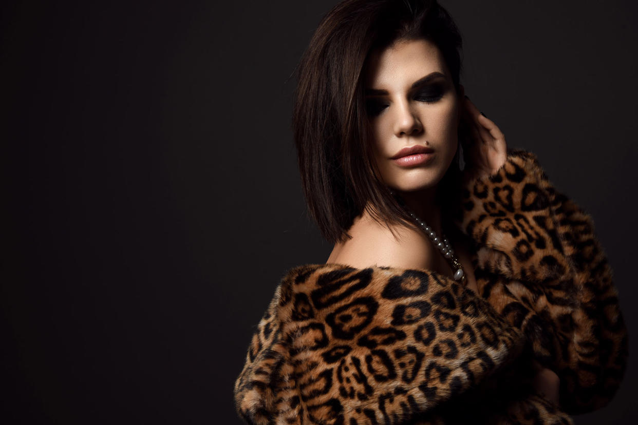 Portrait of young pretty brunette woman model in leopard fur coat with naked shoulders in pearl necklace looking down