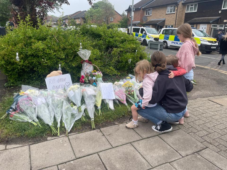 A woman with small children crouches down to read cards left amongst the floral tributes at Laing Close in Hainault for 14-year-old Daniel Anjorin (Samuel Montgomery/PA Wire)