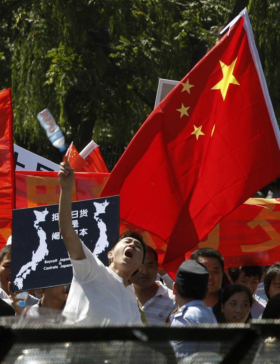 An anti-Japan protester throws a water bottle towards the Japanese Embassy while other protesters march on a street outside the embassy in Beijing, China, Tuesday, Sept. 18, 2012. The 81st anniversary of a Japanese invasion brought a fresh wave of anti-Japan demonstrations in China on Tuesday, with thousands of protesters venting anger over the colonial past and a current dispute involving contested islands in the East China Sea. (AP Photo/Alexander F. Yuan)