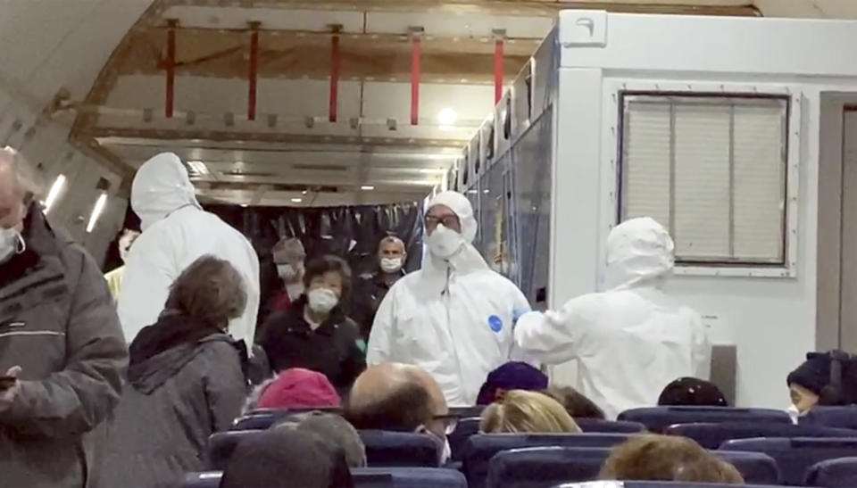 In this image from a video taken on Monday, Feb. 17, 2020, U.S. passengers who evacuated off the quarantined cruise ship the Diamond Princess and officials wait for the takeoff of a Kalitta Air airplane bound for the U.S., at Haneda airport in Tokyo.(Cheryl and Paul Molesky via AP)