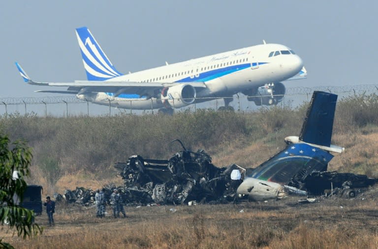 An aircraft takes off near the wreckage of a US-Bangla Airlines plane that crashed in a football field near Kathmandu airport