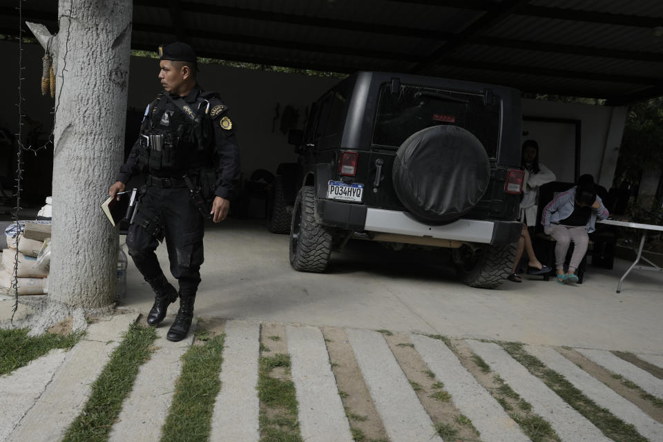 Un policía guatemalteco camina cerca de presuntos traficantes de migrantes, a la derecha, quienes fueron detenidos durante una operación contra una supuesta red de "coyotes" en Huehuetenango, Guatemala, cerca de la frontera con México, el martes 2 de agosto de 2022. (AP Foto/Moisés Castillo)