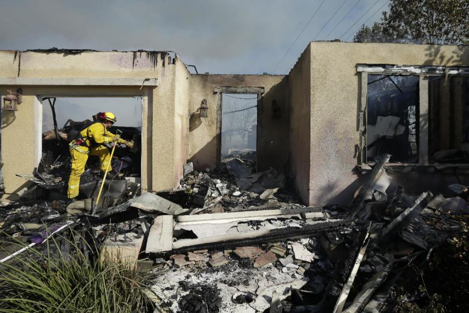 A firefighter removes debris in a burned home during a wildfire Wednesday, May 14, 2014, in Carlsbad, Calif. Flames engulfed suburban homes and shot up along canyon ridges in one of the worst of several blazes that broke out Wednesday in Southern California during a second day of a sweltering heat wave, taxing fire crews who fear the scattered fires mark only the beginning of a long wildfire season. (AP Photo)