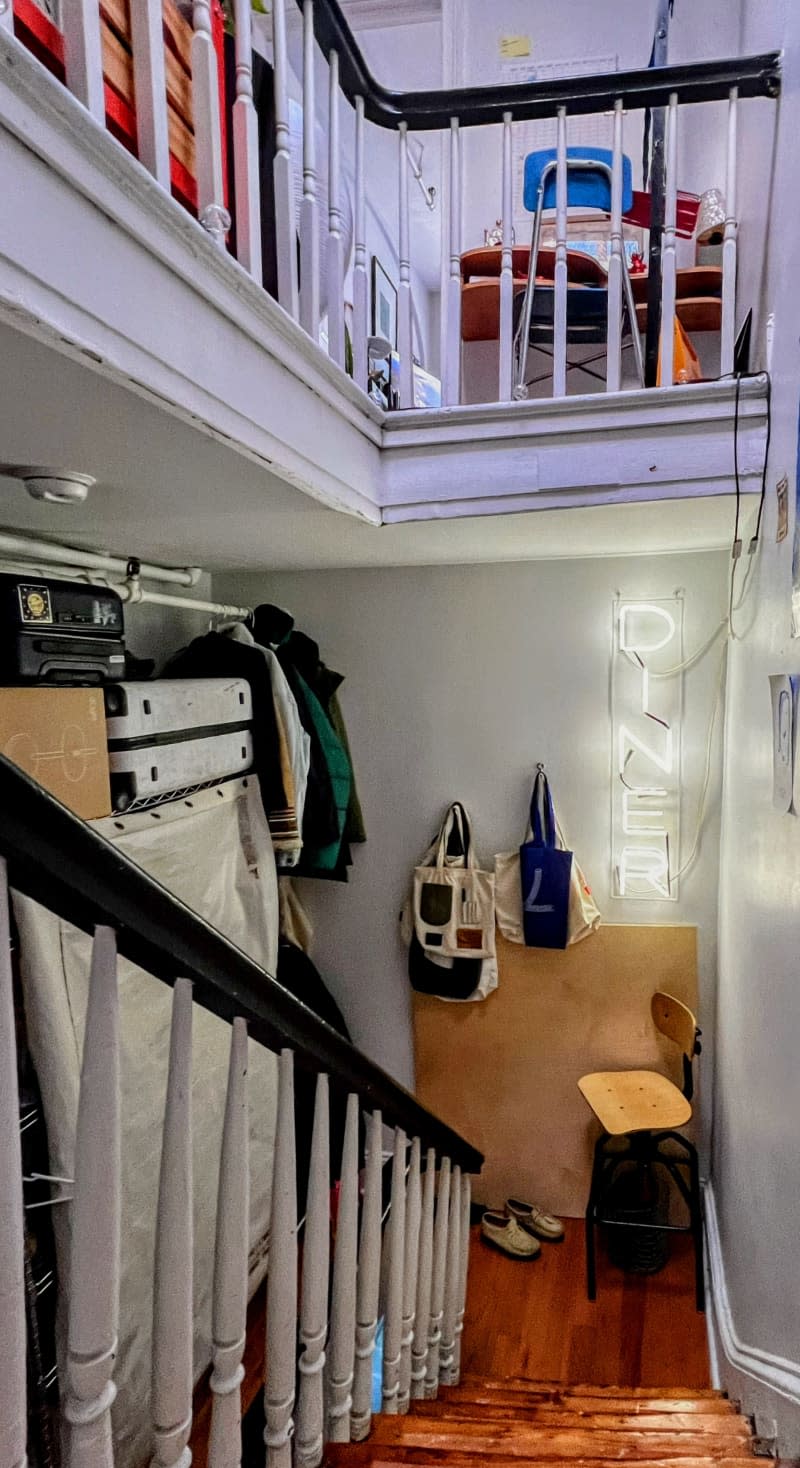 Stairwell with storage, neon diner sign, and a blue desk chair next to a ladder with decorative flags hanging on it.