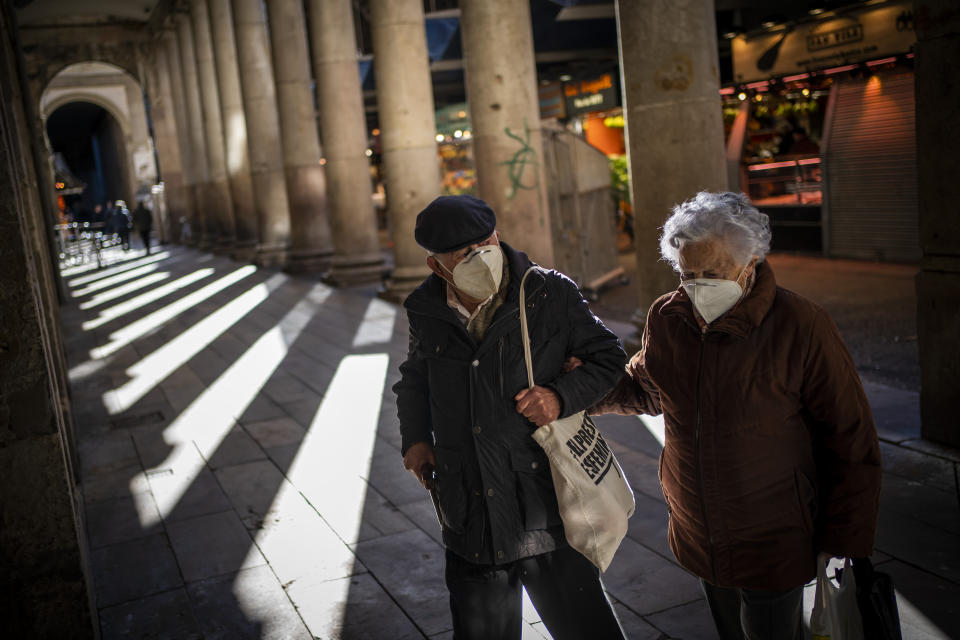 A couple wearing face masks against the spread of Coronavirus walk in a market in Barcelona, Spain, Friday, Jan. 22, 2021. Although health authorities believe that the surge of coronavirus infections is waning, the rate of contagion has shot to over three times the extreme risk level, dangerously straining the health system. (AP Photo/Emilio Morenatti)