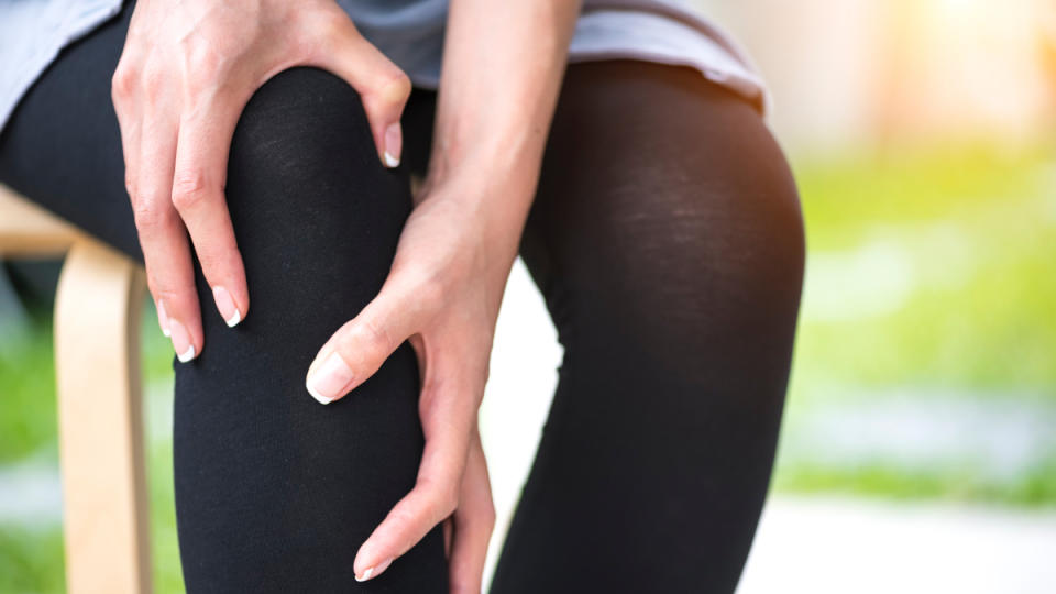 A close up of a woman wearing black pants holding her hands to her knee