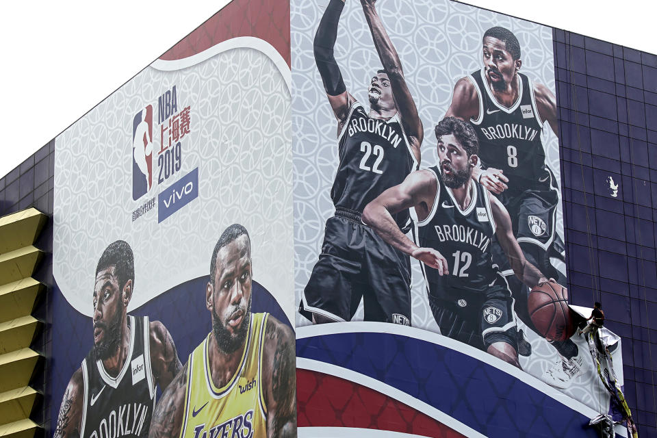 In this Oct. 9, 2019, photo, a worker takes down a billboard advertising an NBA preseason basketball game on Thursday between the Los Angeles Lakers and Brooklyn Nets in Shanghai, China. The NBA has postponed Wednesday's scheduled media sessions in Shanghai for the Brooklyn Nets and Los Angeles Lakers, and it remains unclear if the teams will play in China this week as scheduled. (AP Photo/File)