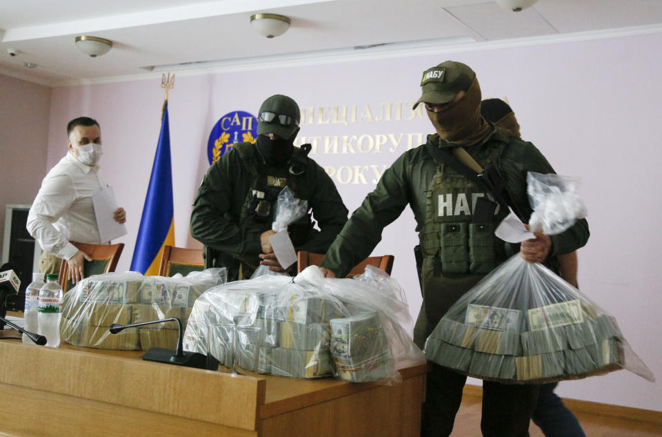 Ukraine's Anti-Corruption Prosecutor Nazar Kholodnytsky, left, watches as police officers hold USD 6 million at a briefing in an anti-corruption prosecutor's office in Kyiv, Ukraine, Saturday, June 13, 2020. Ukrainian authorities say they have intercepted a $6 million bribe attempt at dropping a criminal investigation against the head of the Burisma natural gas company where former US Vice President Joe Biden's son once held a board seat. (AP Photo/Efrem Lukatsky)