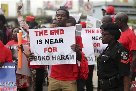 A security officer stands as people hold placards calling for the release of secondary school girls abducted in the remote village of Chibok, during a protest along a road in Lagos May 14, 2014. REUTERS/Akintunde Akinleye