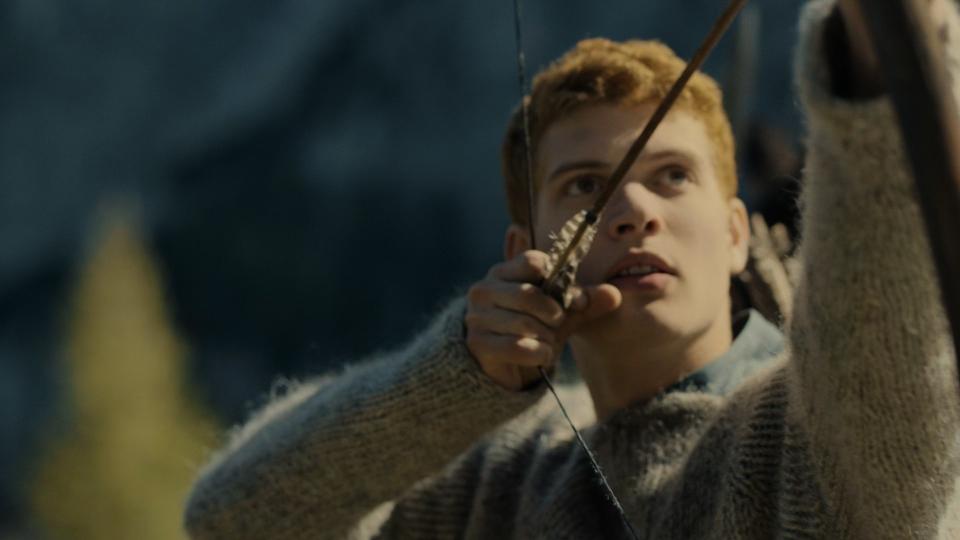 A close-up shot on Rand al’Thor (Josha Stradowski), as he pulls an arrow to his cheek and aims towards the mountainside