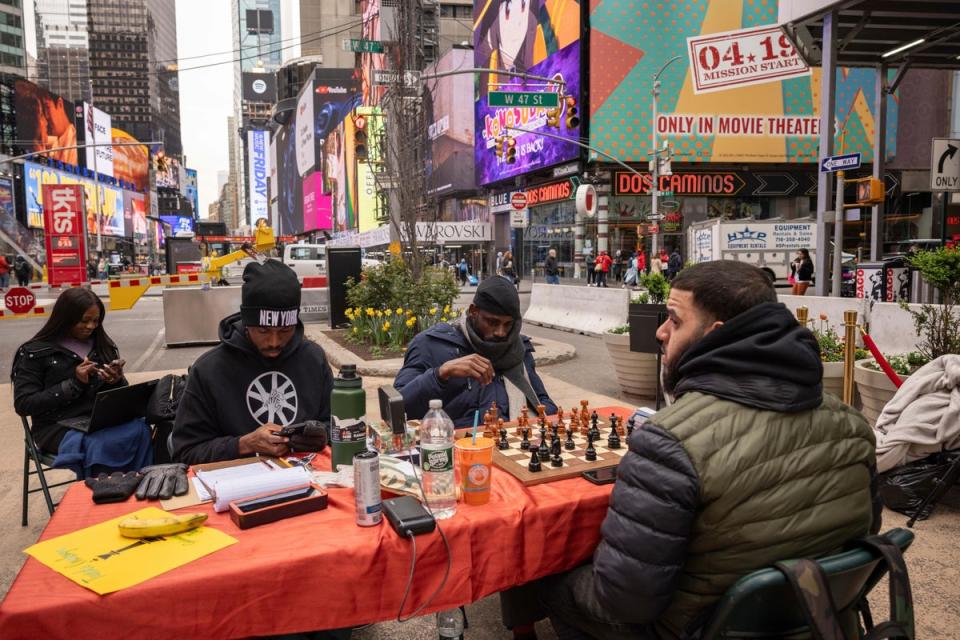 Tunde Onakoya, centre, Nigerian chess champion and child education advocate, plays a chess game in Times Square (AP)