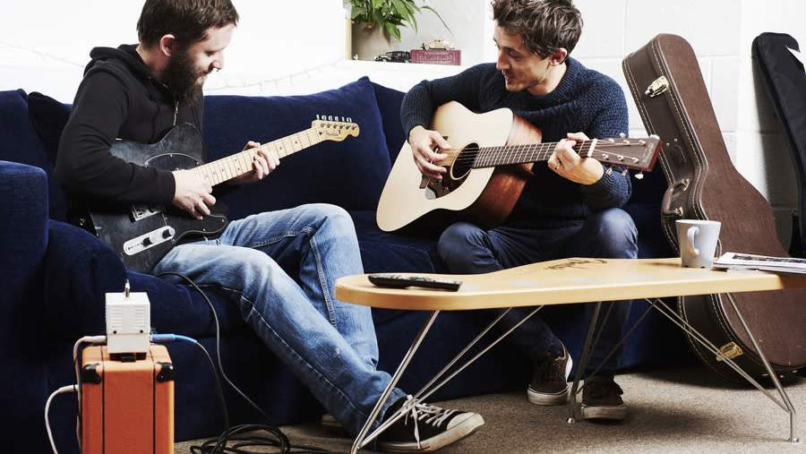  Two guitarists jamming on a sofa. 