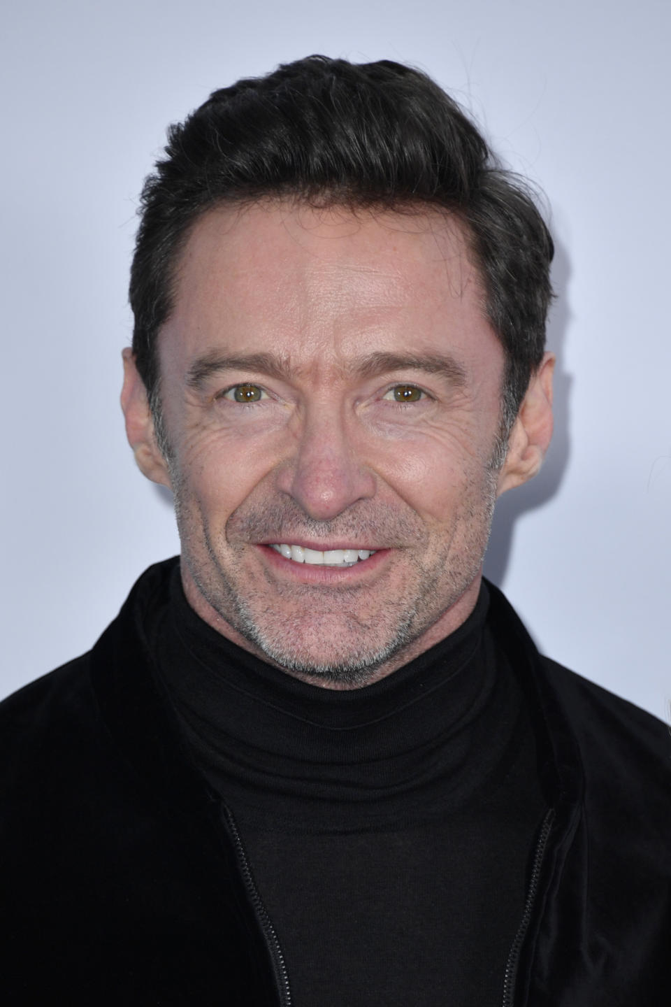 Hugh Jackman smiling at the camera, wearing a black turtleneck