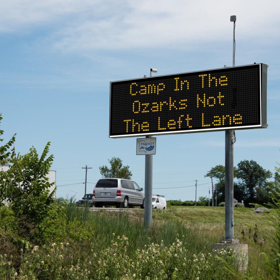 A Missouri Department of Transportation roadside safety sign saying "Camp in the Ozarks, not the left lane."