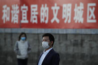 People wearing face masks to help curb the spread of the coronavirus walk by a banner which reads "Harmonious and livable civilized city" on display along a street in Beijing, Tuesday, Oct. 27, 2020. (AP Photo/Andy Wong)