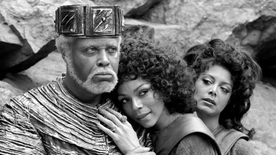 James Earl Jones, with short, white hair and a beard, glares sternly while his two co-stars lean into him.