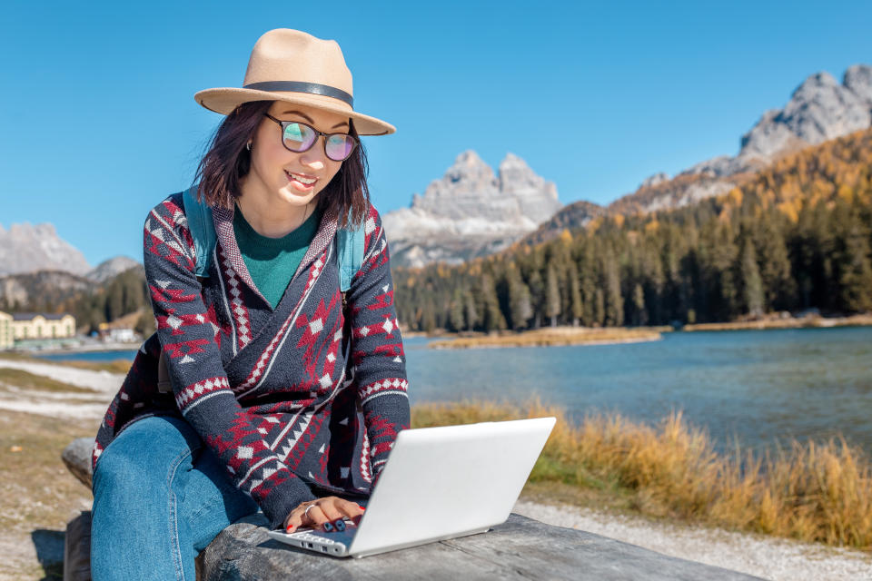 Happy Asian woman working on laptop on mountain lake background in autumn. The concept of remote work and freelancer
