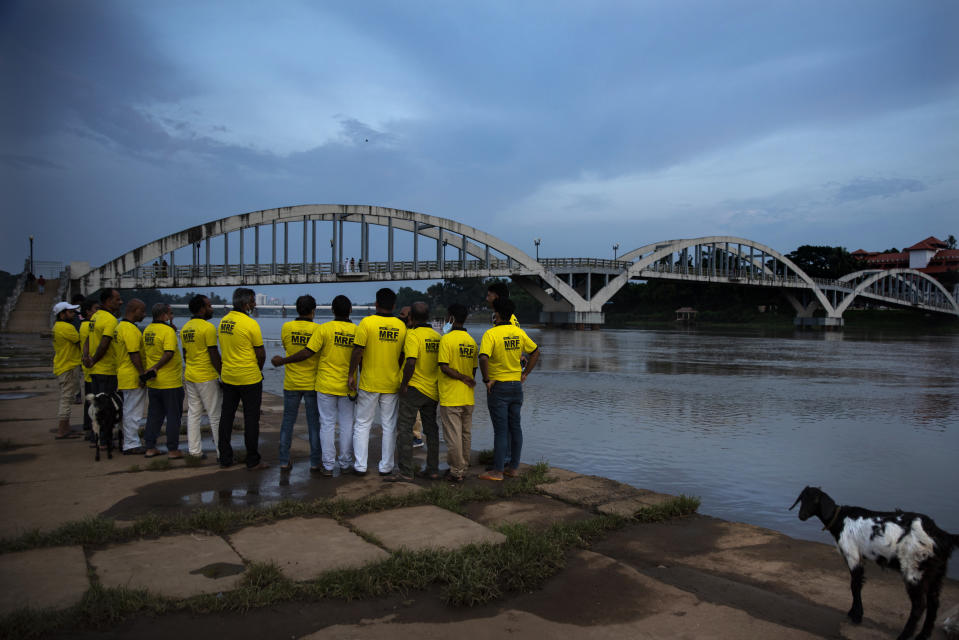 Members of Merchant Rescue Force (MRF) a volunteer group of local traders listen to a brief from their team captain by the Periyar River as they anticipate water levels to rise following opening of gates of the Idukki dam in Kochi, Kerala state, Tuesday, Oct. 19, 2021. Several dams in the state are nearing their full capacity and expecting more rains in the coming days, authorities released water as a precautionary measure. (AP Photo/R S Iyer)