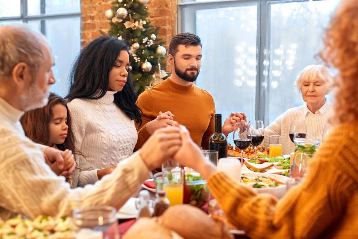 mixed race family holding hands and praying before vegan holiday dinner