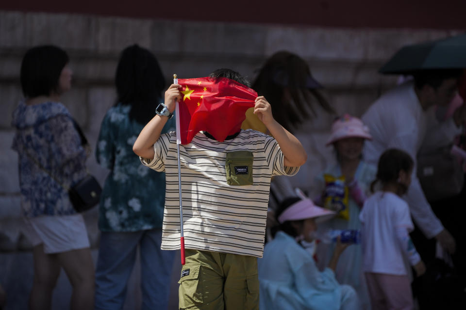 A boy uses a national flag to shield from the sun as visitors line up to enter the Forbidden City on a sweltering day in Beijing, Friday, July 7, 2023. Earth's average temperature set a new unofficial record high on Thursday, the third such milestone in a week that already rated as the hottest on record. (AP Photo/Andy Wong)