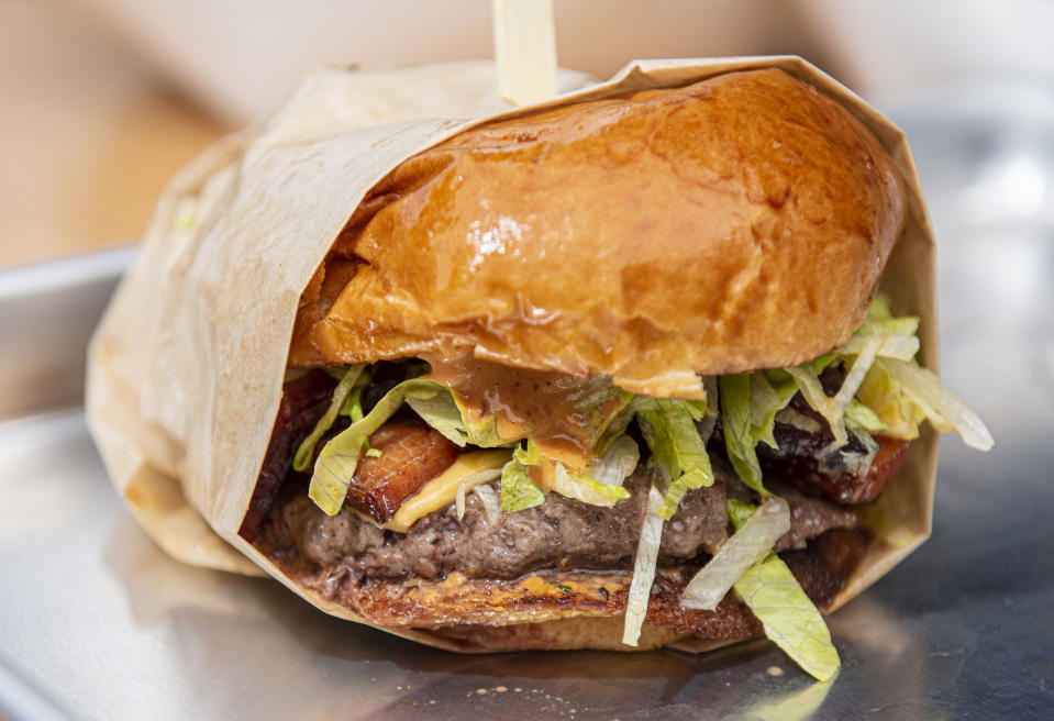 A close-up of a juicy hamburger wrapped in brown paper. It contains a beef patty, lettuce, and sauce on a brioche bun.