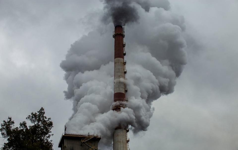 Viewed from below a cloudy sky, a red and white factory chimney billows smoke.