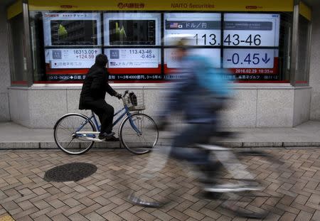 A man riding on a bicycle looks at an electronic board showing the exchange rate between Japanese yen against the U.S. dollar (R), the graphs of its recent fluctuations (C) and the graph of Japan's Nikkei average outside a brokerage in Tokyo, Japan, February 29, 2016. REUTERS/Yuya Shino