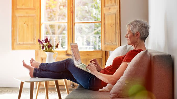 Shot of a mature woman relaxing on her sofa at home using a laptop.