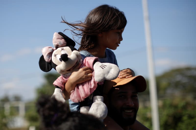 A migrant, part of a group that is mainly from Central America and that travels in a caravan, carries a child as he walks on a road near Frontera Hidalgo, Chiapas