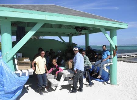 Cuban rafters sit together on the beach after landing on the Cayman Islands, in George Town December 14, 2014. REUTERS/Peter Polack