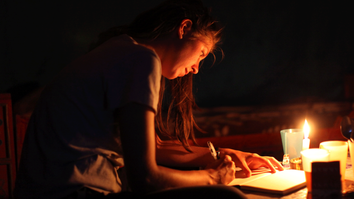 Woman journaling by candlelight as she takes part in a moon circle