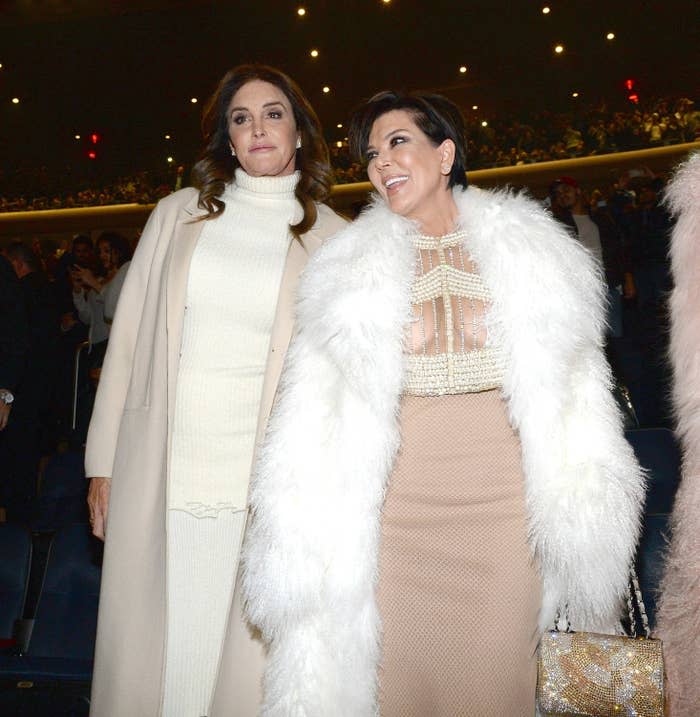 Caitlyn Jenner in a white turtleneck dress and coat, stands next to Kris Jenner in a nude dress and white fur coat at an event. Both women are smiling