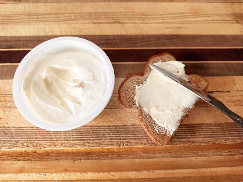 A tub of cream cheese with a slice of bread with cream cheese and knife on it