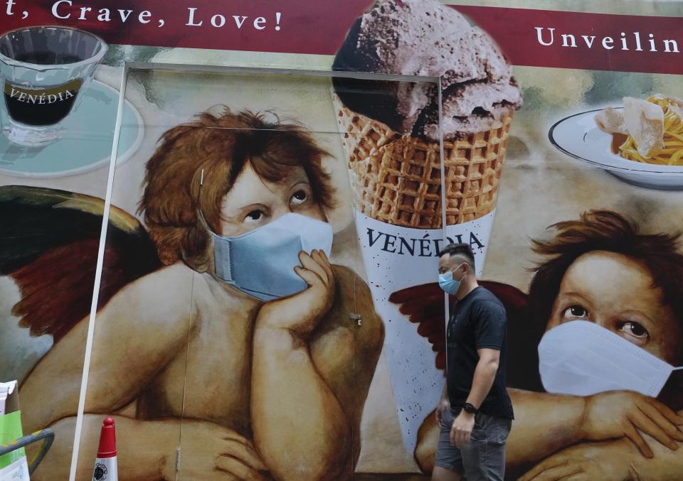 A man wearing a face mask to prevent the spread of the coronavirus walks past a huge poster on a street in Hong Kong, Wednesday, May 12, 2021. (AP Photo/Vincent Yu)