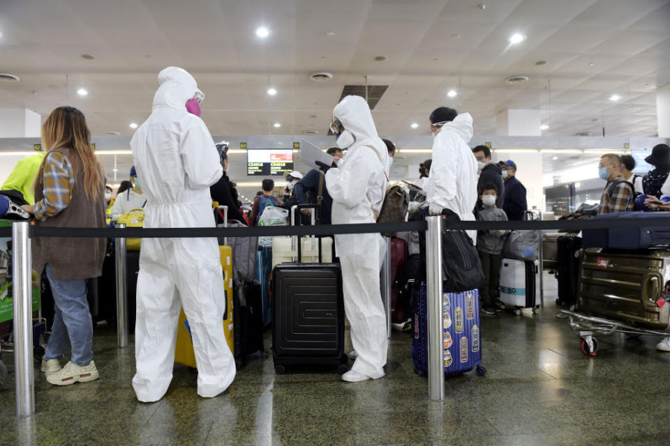 Melbourne Airport passengers wearing protective masks and hazmat suits with their luggage in tow.