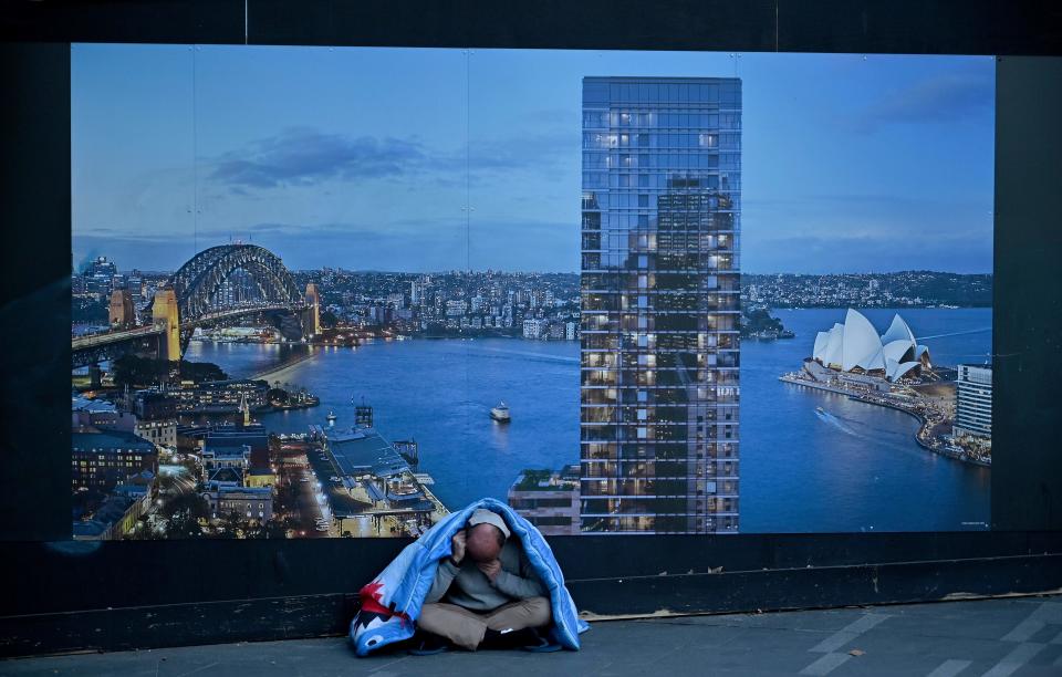 A homeless man sits in front of a billboard by a construction site in Sydney on July 24, 2019. (Photo by PETER PARKS / AFP)        (Photo credit should read PETER PARKS/AFP via Getty Images)