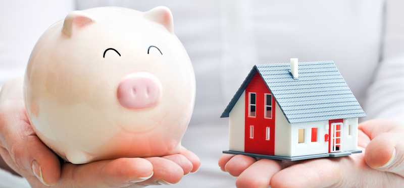 Hands holding piggy bank in one hand and model home in the other.