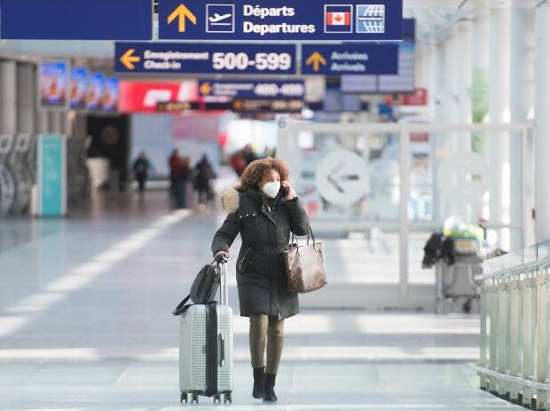 An air passenger wears a face mask while walking through Montreal–Trudeau International Airport in December 2020. People are already booking vacations to overseas locations, but one epidemiologist says global travel won't be back to normal until at least 2024.  (Graham Hughes/CP - image credit)