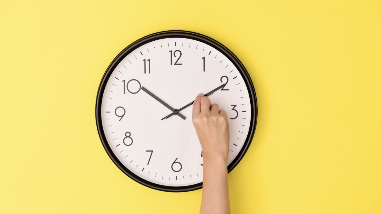  Somebody adjusting the minute hand on a clock hanging on a yellow wall. 