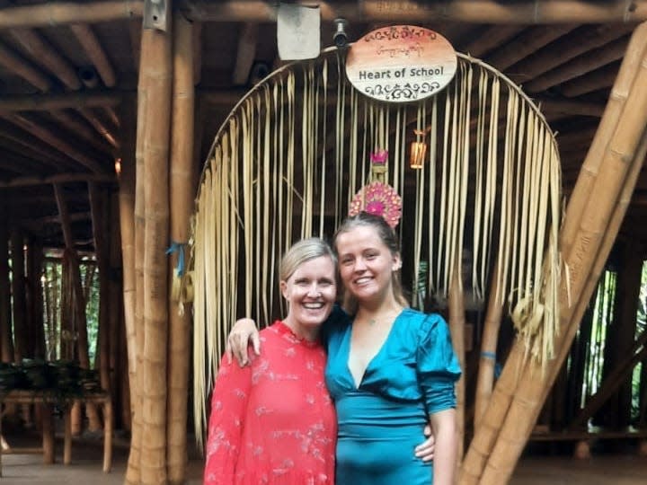 A woman in a red dress and a young girl in a blue dress in front of a bamboo building in Bali.