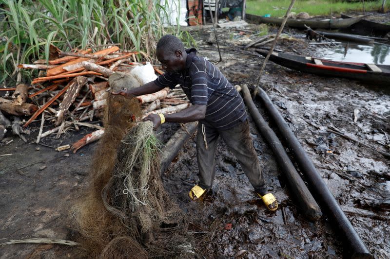 Benson Daniel, Community Development Chairman, Sandsand fishing settlement, holds up oil-soaked fishing net at Sandsand settlement, in Nembe, Bayelsa