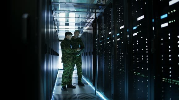 Two military officers stand between rows of mainframe computers in a data center.