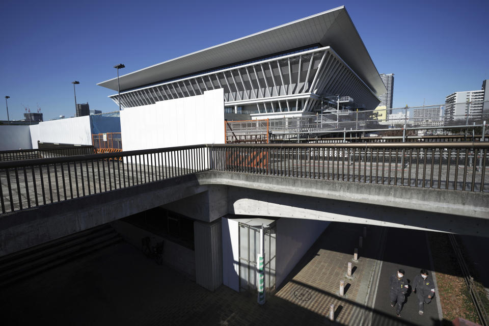 Two men walk near the Tokyo Aquatics Center, one of the venues of Tokyo 2020 Olympic and Paralympic games, in Tokyo Wednesday, Jan. 20, 2021. The postponed Tokyo Olympics are to open in just six months. Local organizers and the International Olympic Committee say they will go ahead on July 23. But it’s still unclear how this will happen with virus cases surging in Tokyo and elsewhere around the globe. (AP Photo/Eugene Hoshiko)