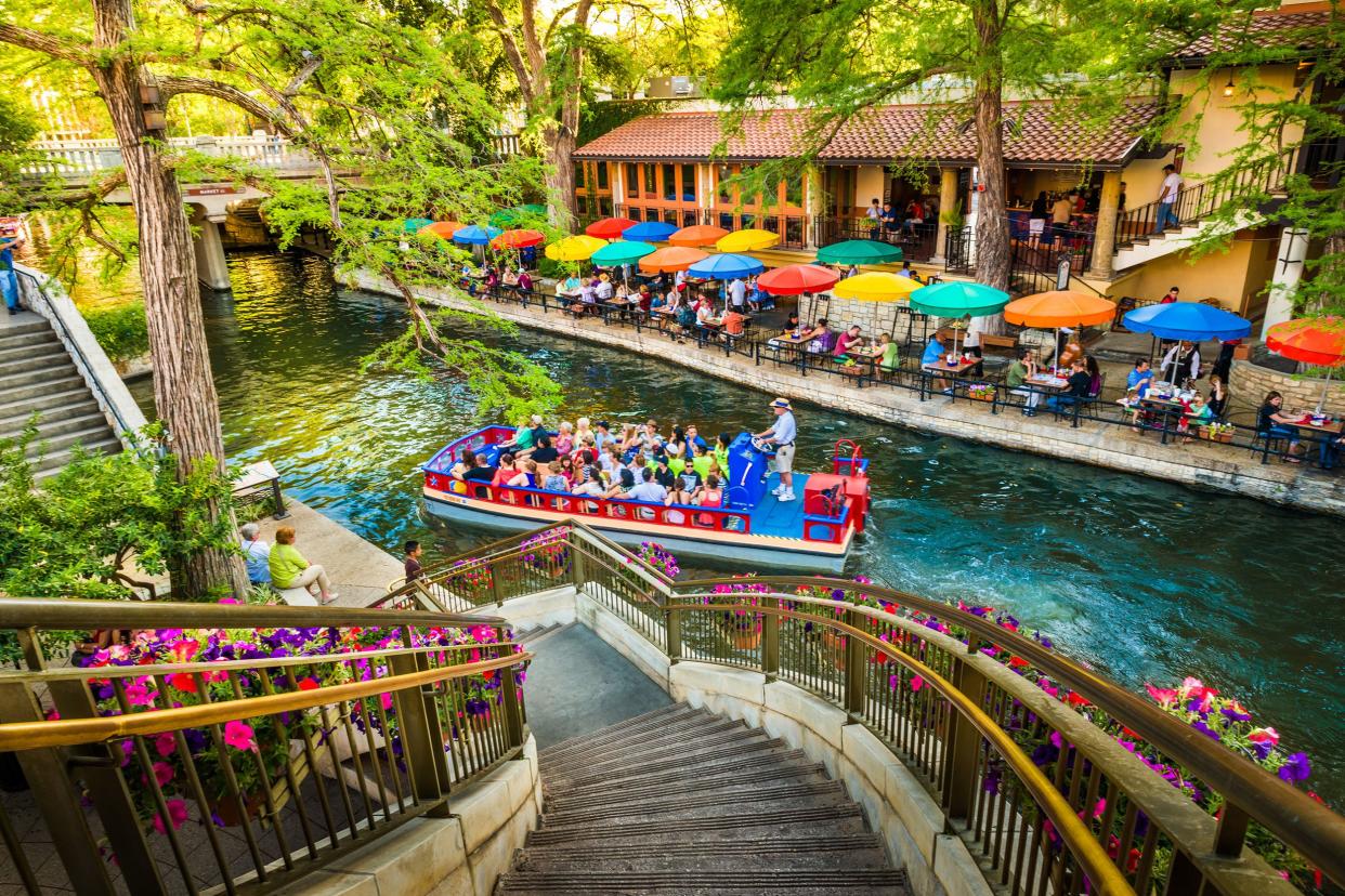 River Walk, San Antonio, Texas with boat in the center and colorful array of umbrellas on resturant tables lining the river