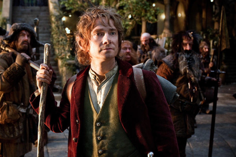 Bilbo Baggins stands with a walking stick in front, dwarves behind him in a scene from The Hobbit