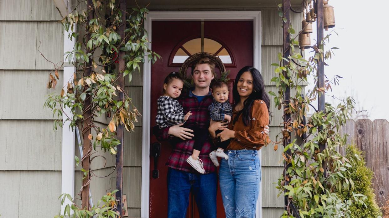 a cute multiracial young family with two kids hangs a christmas wreath on their front door shot in portland oregon