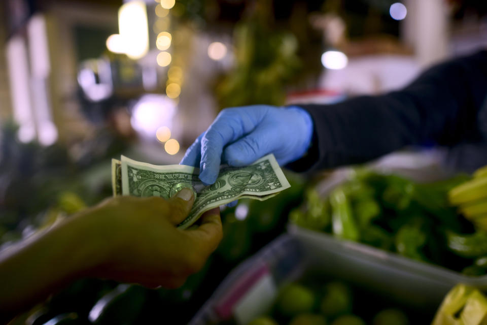 Jorge Otero, owner of a fruit and vegetables stand, wears gloves as he exchanges cash with a customer, during a government curfew aimed at curbing cases of the new coronavirus that has shuttered all non-essential businesses for two weeks in San Juan, Puerto Rico, Thursday, March 19, 2020. (AP Photo/Carlos Giusti)