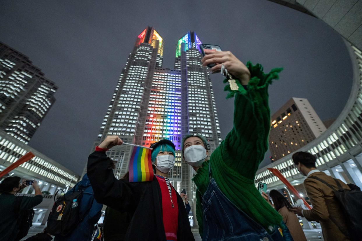 A couple take a selfie in front of the Tokyo Metropolitan Government building, illuminated with rainbow lights, in Shinjuku district of Tokyo, November 1, 2022, as Tokyo began issuing partnership certificates to same-sex couples who live and work in the capital. / Credit: YUICHI YAMAZAKI/AFP/Getty